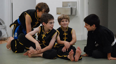 Young martial arts students smile and talk in front of a water fountain at the Woodward dojo.